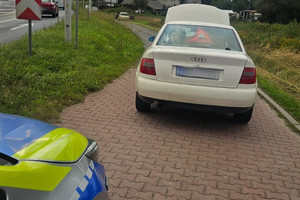 Na zdjęciu widać biały samochód oraz radiowóz i zjazd z drogi.