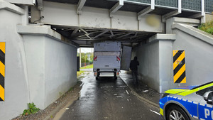 Na zdjęciu widać samochód dostawczy zakleszczony pod kolejowym wiaduktem oraz radiowóz Policji.