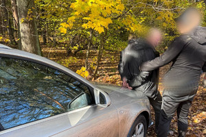 Na zdjęciu widać policjanta oraz zatrzymanego mężczyznę prowadzonego przez las.