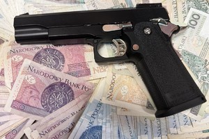 Na zdjęciu widać przedmiot przypominający broń na tle banknotów