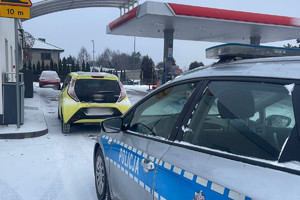 Na zdjęciu widać radiowóz na stacji paliw oraz jasny samochód.