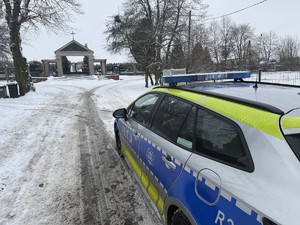 Na zdjęciu widać policyjny radiowóz a w tle cmentarz.