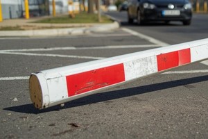 Grafika przedstawia uszkodzony szlaban leżący na jezdni, obok jezdnię i nadjeżdżający pojazd.