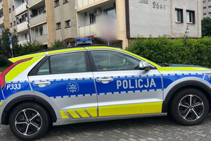 Na zdjęciu widać policyjny radiowóz, a w tle bloki i osiedle.