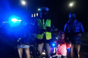 policjantka i dzieci z odblaskami na tle radiowozu