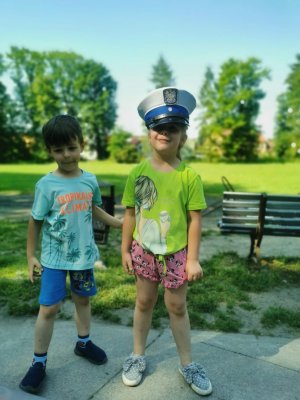 dwoje dzieci stoi obok siebie dziewczynka i chłopczyk dziewczynka ma założoną czapkę policyjną