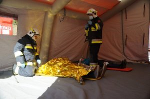 wnętrze namiotu w którym znajdują się osoby poszkodowane oraz strażacy udzielający im pomocy