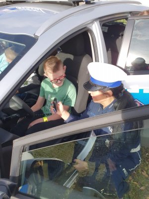 ucze4ń siedzi za kierownicą radiowozu obok niego kuca policjantka
