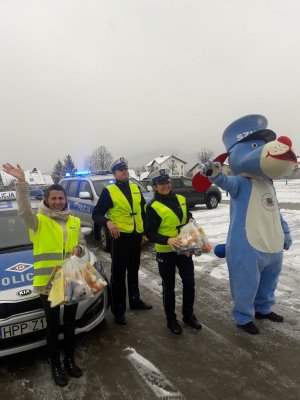 uczestnicy akcji trzymają paczki i machają dzieciom