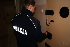 zdjęcie poglądowa fragment policjanta zamykającego drzwi do pomieszczenia dla osób zatrzymanych