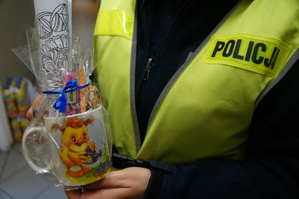 fragment policjantki która trzyma kubek z kolorowanką i słodyczami