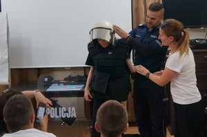 policjant i opiekunka przymierzają chłopakowi policyjne wyposażenie
