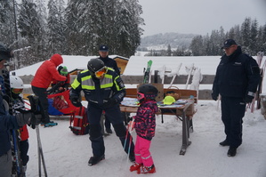 policjant narciarz uczy jazdy na nartach dziewczynkę w tle stoi dwóch innych policjantów