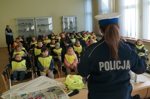 policjantka stoi tyłem przed nią na krzesłach siedzą dzieci