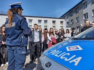 zdjęcie kolorowe na pierwszym planie policjantka i fragment radiowozu w tle uczniowie