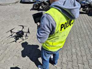 Zdjęcie kolorowe: fragment sylwetki policjanta, obok którego na ziemi znajduje się dron