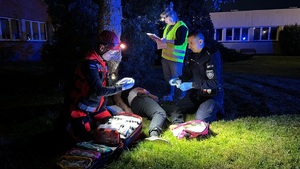 zdjęcie kolorowe zrobione w nocy policjant oraz ratownicy w czasie udzielania pomocy