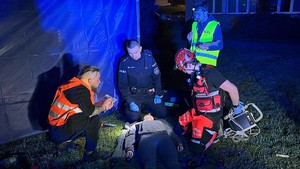 zdjęcie kolorowe zrobione w nocy na ziemi leży poszkodowany obok policjant i ratownicy udzielają mu pomocy