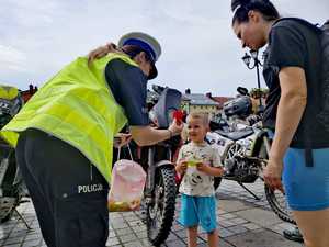 zdjęcie kolorowe policjantka wręcza dziecku zawieszkę odblaskową obok motory