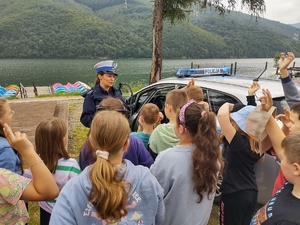 policjantka prowadzi prelekcję dzieci stoją tyłem obok radiowóz