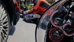 zdjęcie na którym widać fragment samochodu, motocykla oraz samochodu w tle leżącego na jezdni motocyklistę