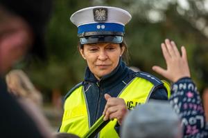 zdjęcie kolorowe przedstawiające policjantkę rozdającą odblaski dzieciom