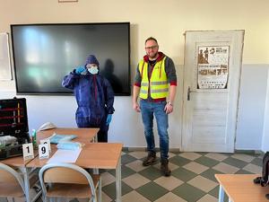 zdjęcie kolorowe, sala lekcyjna, technik stoi na środku, obok niego uczeń ubrany w strój ochronny