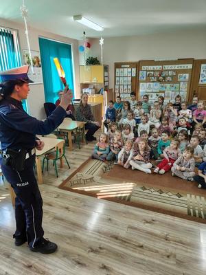 zdjęcie kolorowe policjantka stoi na środku sali, dzieci siedzą na podłodze