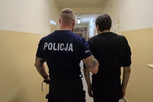 policjant stoi z zatrzymanym, obaj stoją tyłem