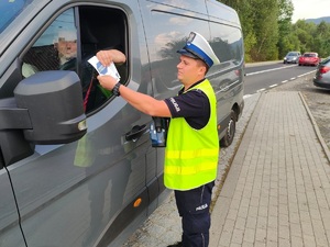 zdjęcie kolorowe, policjant rozdaje ulotkę kierującemu