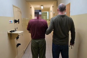 Zdjęcie przedstawia zatrzymanego mężczyznę prowadzonego przez policjanta