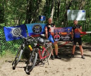 Sierżant sztabowy Damian Lorisz z towarzyszem wyprawy Piotrem z rowerami i w strojach rowerowych, z flagami związkowymi i plakatem promującym wydarzenie, na granicy polsko-rosyjskiej.