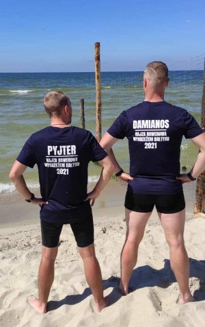 Sierżant sztabowy Damian Lorisz z towarzyszem wyprawy Piotrem w okolicznościowych koszulkach z nazwą przedsięwzięcia, na plaży na tle Morza Bałtyckiego.