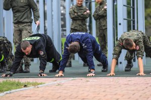 Trzy osoby w mundurach wojskowych, straży pożarnej i policyjnych w podporze prostym przygotowani do ćwiczeń.