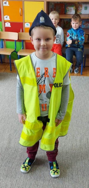 Chłopiec ubrany w kamizelkę odblaskową z napisem Policja i furażerkę z umundurowania ćwiczebnego.