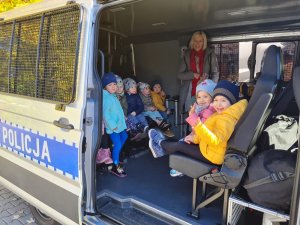 Ośmioro dzieci z wychowawczynią siedzą wewnątrz radiowozu typu furgon.