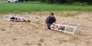 2 zawodników czołga się w piachu pod wąskimi tunelami z metalowych prętów.