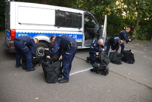5 policjantów przy radiowozie służbowym typu furgon w pośpiechu ubiera się w sprzęt PZ.