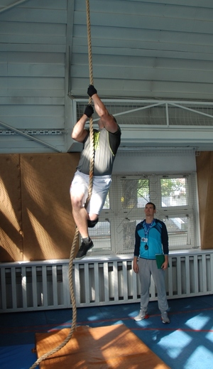 Uczestnik zawodów podczas wejścia na linę zawieszoną do sufitu hali sportowej. W tle sędzia.