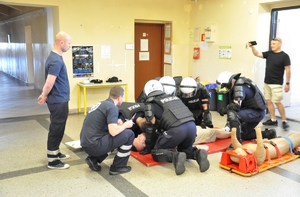 Policjanci w sprzęcie PZ udzielają pomocy rannemu w pomieszczeniach kompanii.