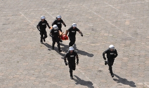 Policjanci w sprzęcie PZ biegną z manekinem na desce. Widok z góry.