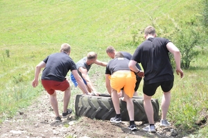 Zawodnicy sprowadzają oponę z ciągnika rolniczego w dół wzniesienia.