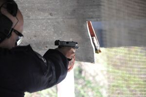 Policjant oddaje strzał. Ujęcie od tyłu. Zbliżenie na broń - zamek w tylnym położeniu, widoczna smuga dymu na wylocie z lufy.