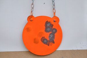 Zbliżenie na gong pomalowany pomarańczową farbą, z widocznymi śladami po pociskach.