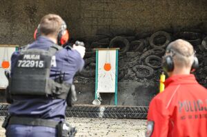 Policjant i sędzia podczas konkurencji strzelania do gongu. Ujęcie od tyłu.