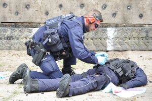 Policjant udziela pomocy (zakłada stazę taktyczną na krwawiące udo) rannemu policjantowi - realistycznie ubranemu i ucharakteryzowanemu manekinowi.