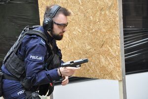Policjant przy przysłonie z przechyloną bronią z zamkiem w tylnym położeniu. W komorze nabojowej widoczny nabój.