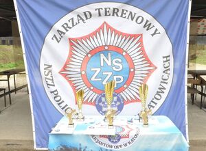 Puchary, statuetki i dyplomy na stoliku na tle flagi związkowej.