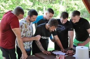Zawodnicy skupiają się nad kartką z zapisanymi działaniami matematycznymi do zapamiętania.