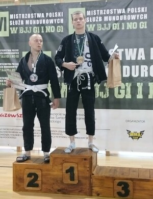 Starszy posterunkowy Oskar Kudzia ze złotym medalem i dyplomem na najwyższym stopniu podium. Na miejscu drugim kolejny zawodnik.